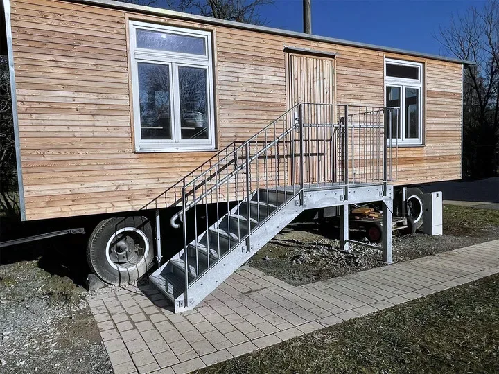 Feuerverzinkte Treppe mit Podest und Geländer an einem holzverkleideten Zirkuswagen