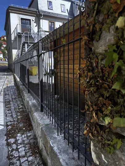 Stabzaun mit Spitzen auf einer Natursteinmauer
